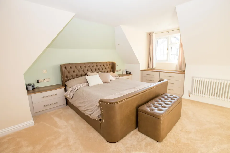 Converted loft bedroom with sloping ceiling and an upholstered bed
