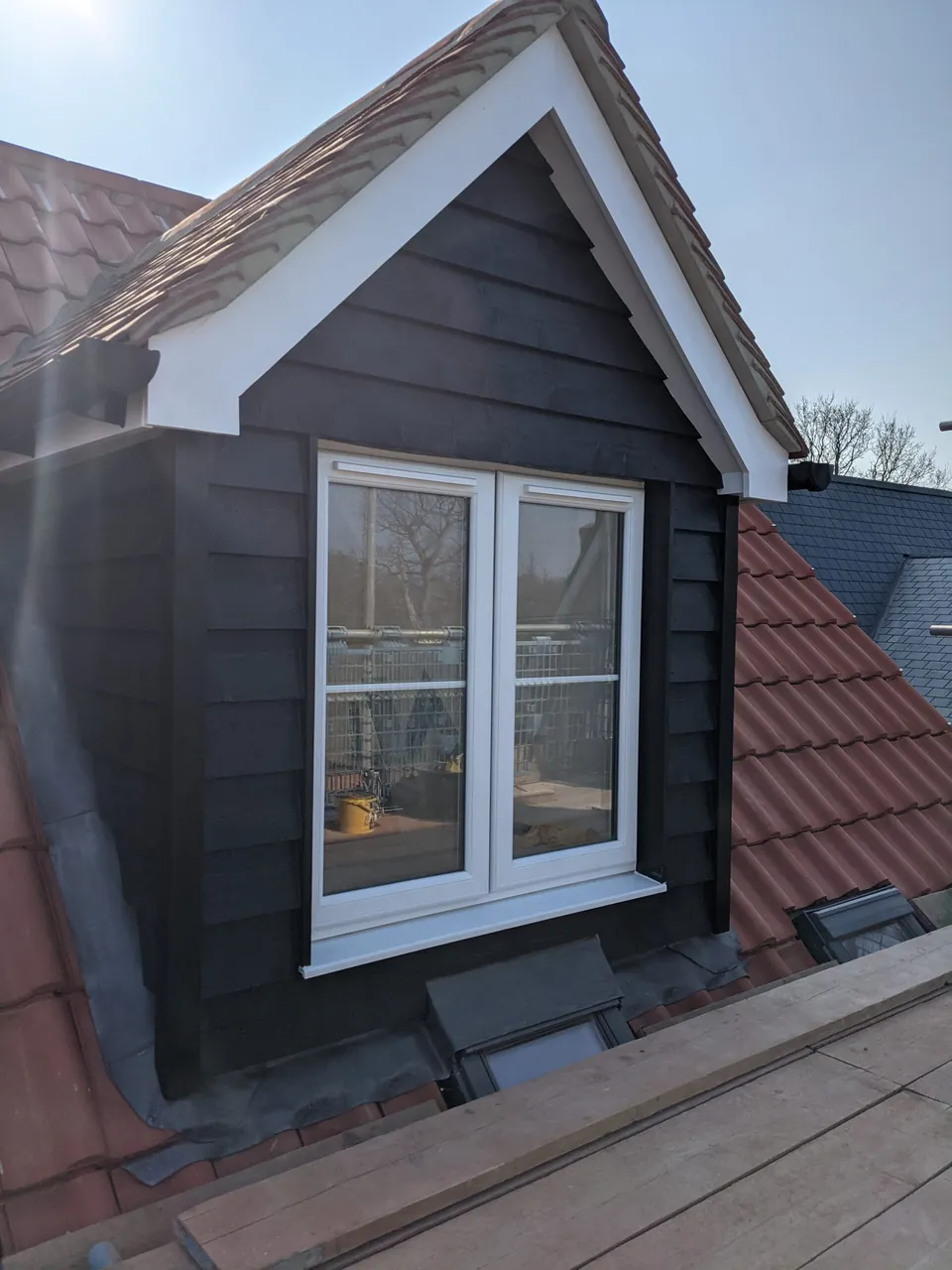 Close view of a black timber dormer with white trim and a white casement window